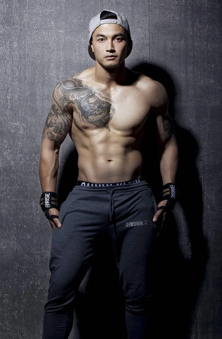 Michael Le in a Wink Models portfolio photograph, 2016. Backwards cap, dragon tattoo across the shoulder and chest, grey sweatpants, against a concrete wall.